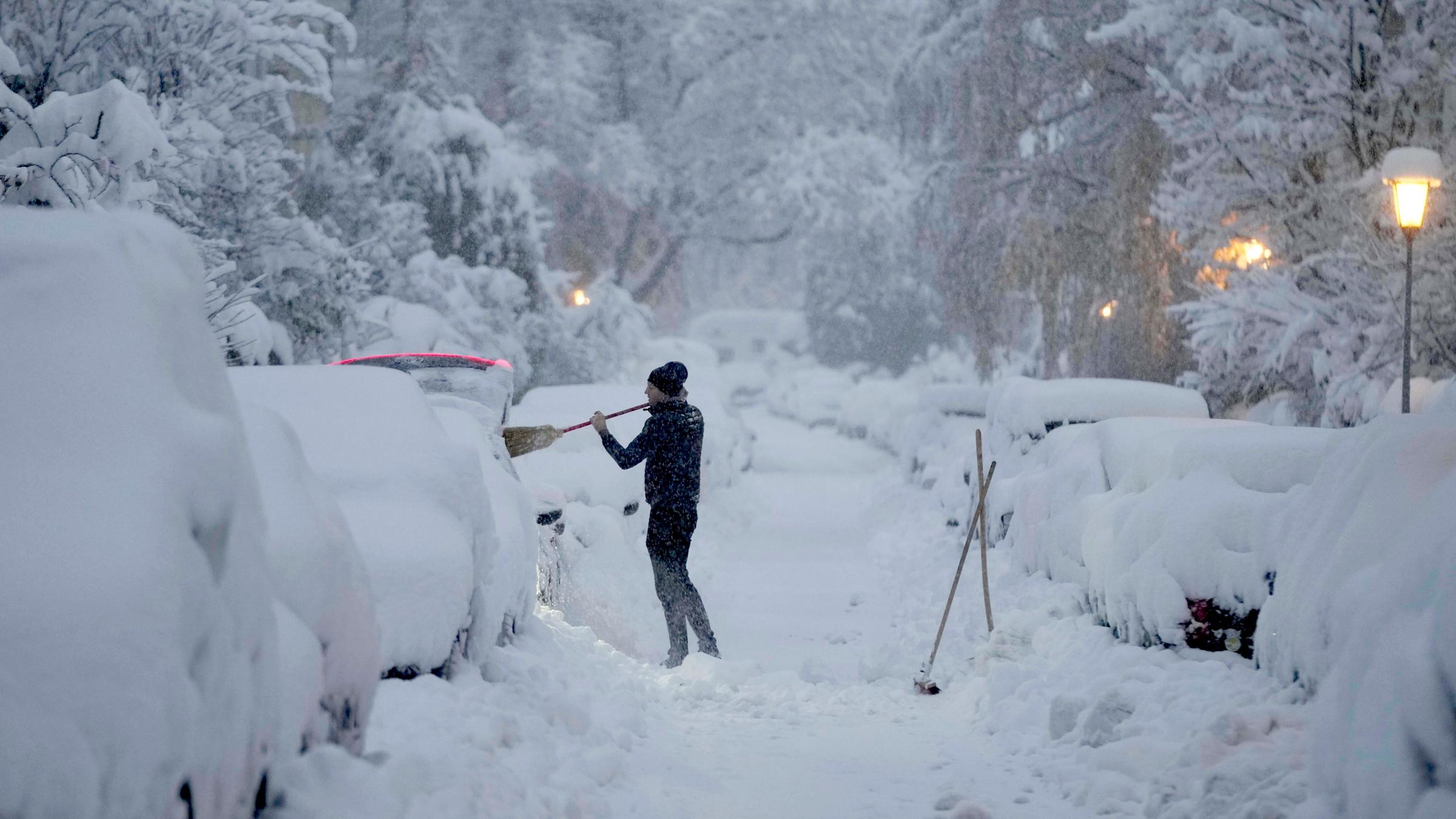 Ein Mann befreit sein Auto in München von Schneemassen.