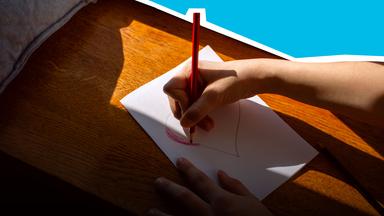 Kind zeichnet mit Buntstift ein rotes Herz.