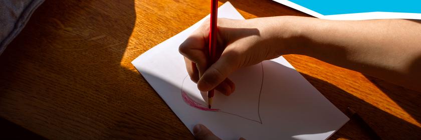 Kind zeichnet mit Buntstift ein rotes Herz.
