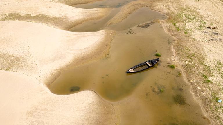 Gelber Sand und ein paar Wasserlachen sind von oben fotografiert. Im Wasser liegt ein Kanu. 