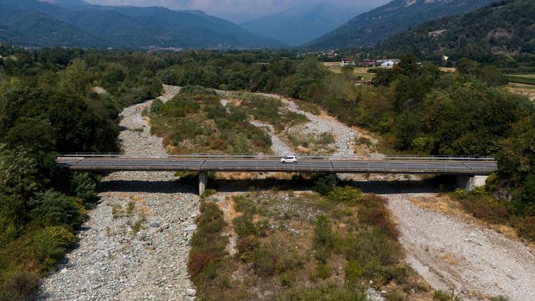 Eine lange Brücke, über die ein Auto fährt, führt über ein breites Flussbett, in dem kein Wasser zu sehen ist. 