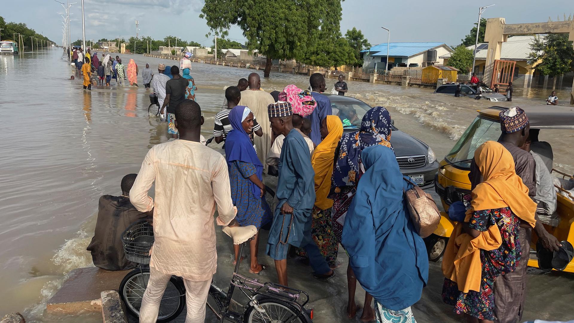 Menschen in Nigeria verlassen auf überfluteter Straße ihr Zuhause 