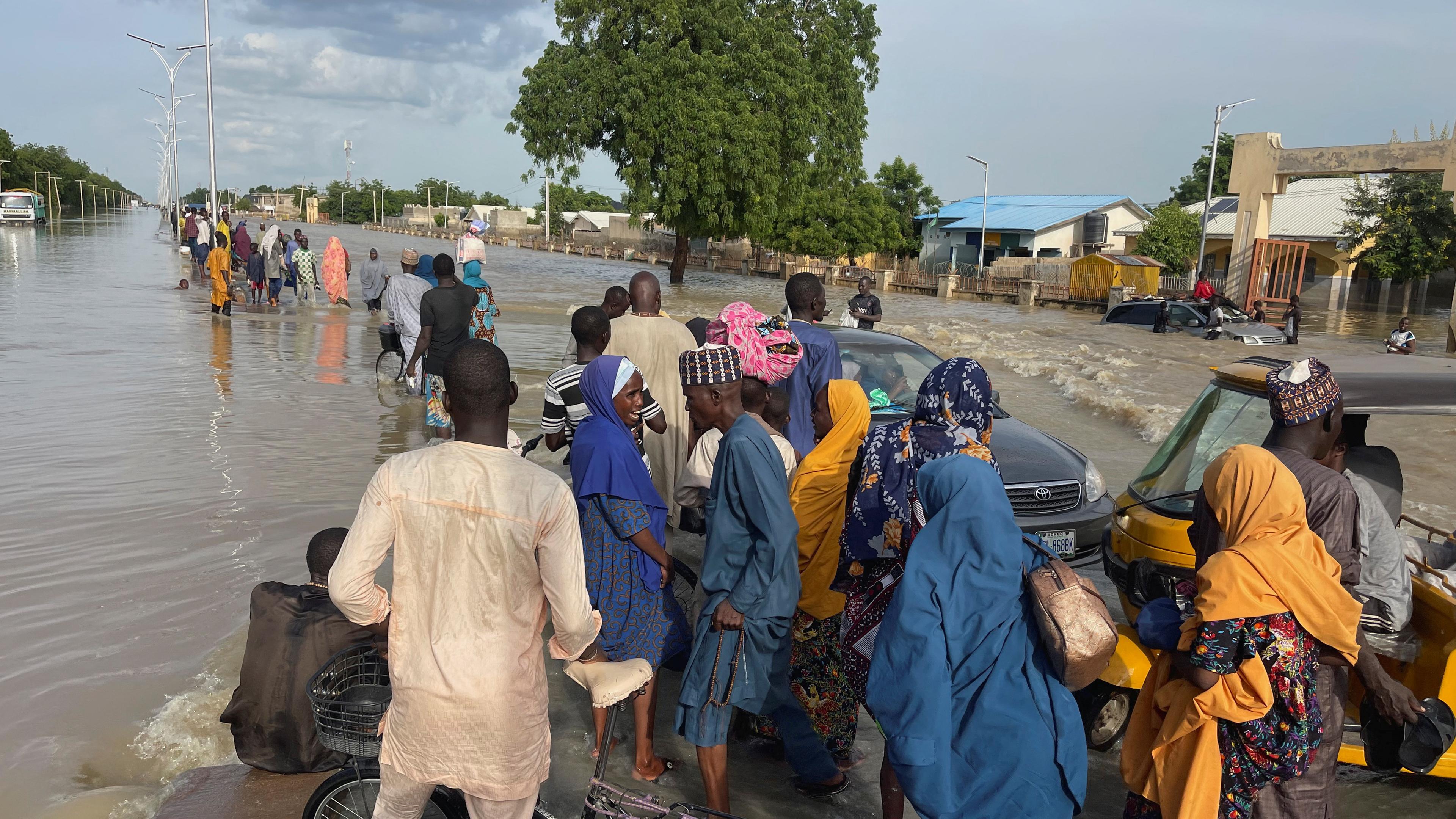 Menschen in Nigeria verlassen auf überfluteter Straße ihr Zuhause 