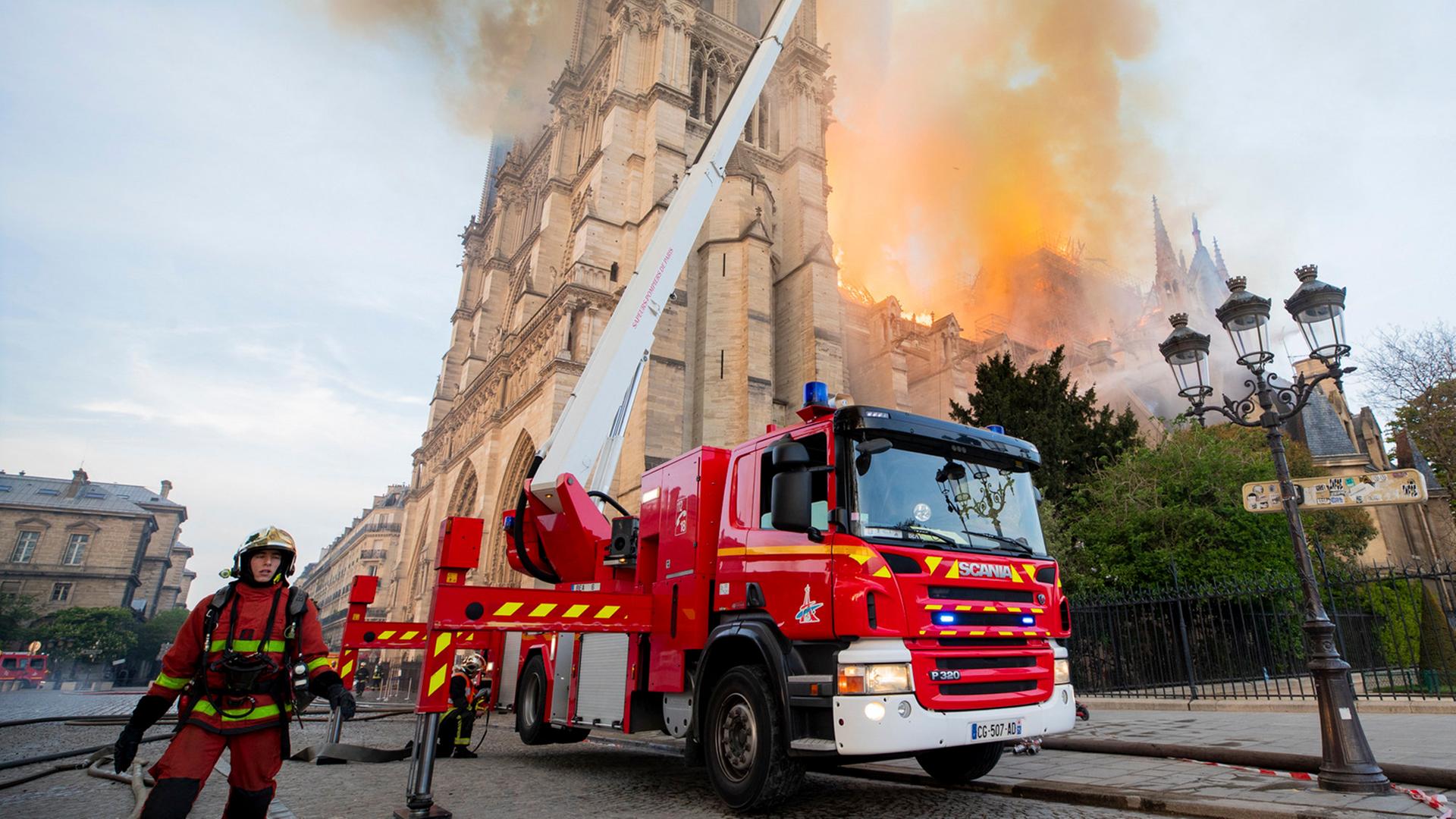 Ein Feuerwehrmann steht neben einem Feuerwehrauto mit ausgefahrener Leiter, von der aus das Feuer in der Notre-Dame gelöscht wird.