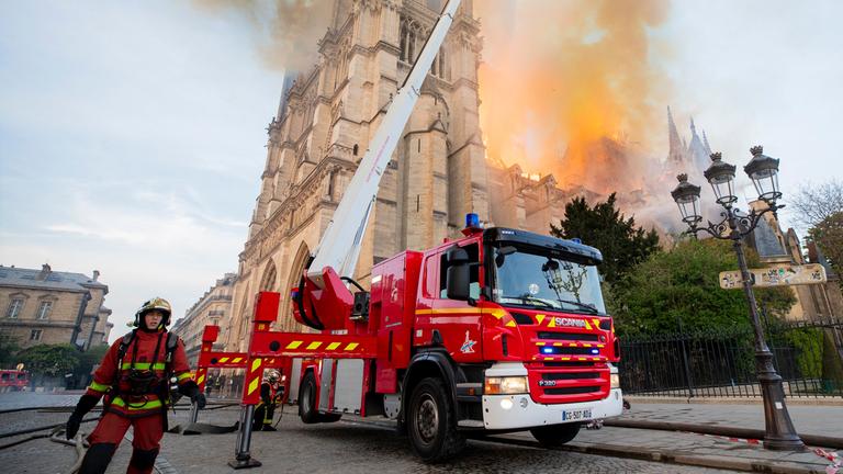 Ein Feuerwehrmann steht neben einem Feuerwehrauto mit ausgefahrener Leiter, von der aus das Feuer in der Notre-Dame gelöscht wird.