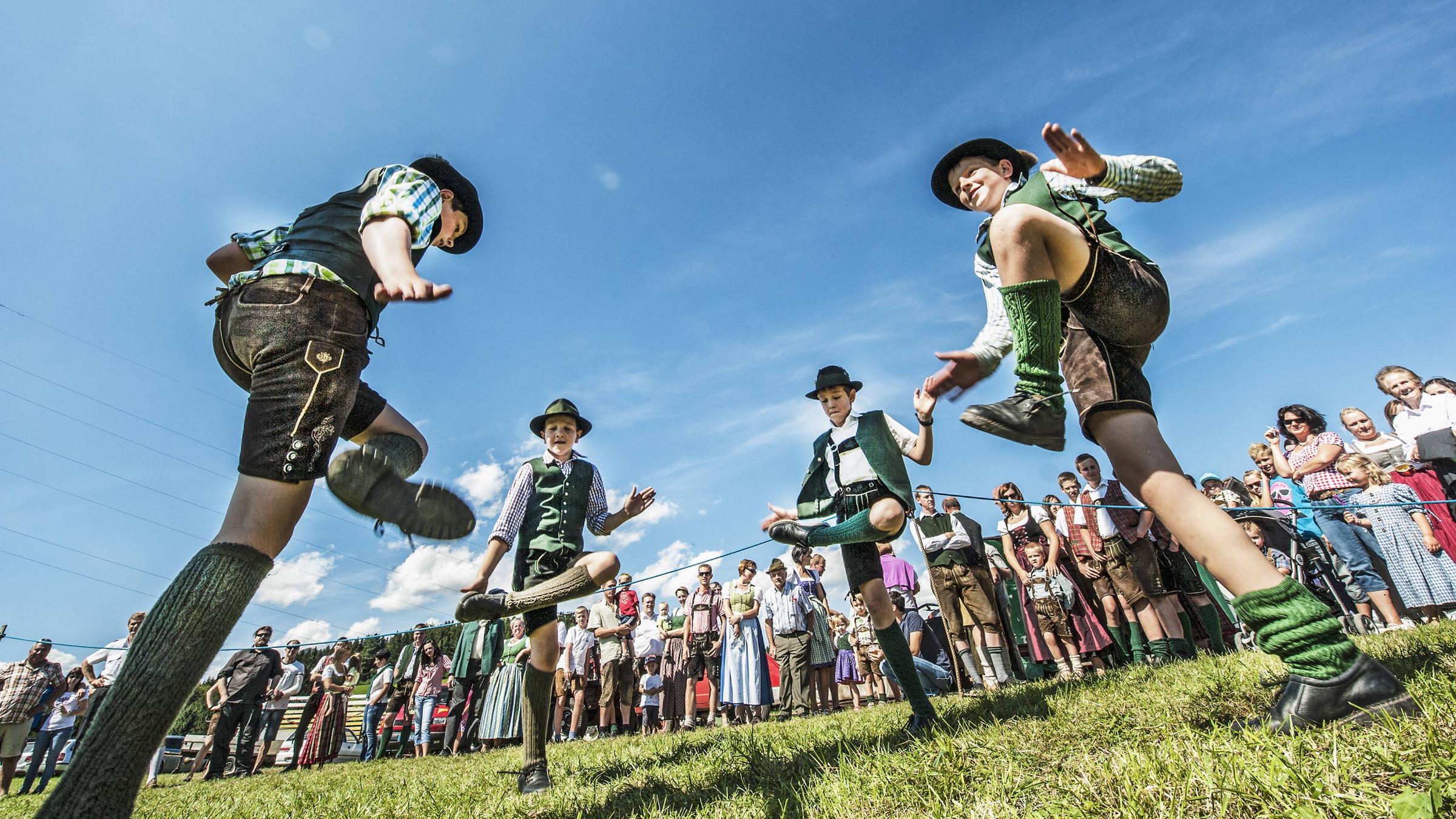 Vier Jungs tanzen in Ledertrachten einen Schuhplattler und klopfen sich dabei auf die Schenkel.