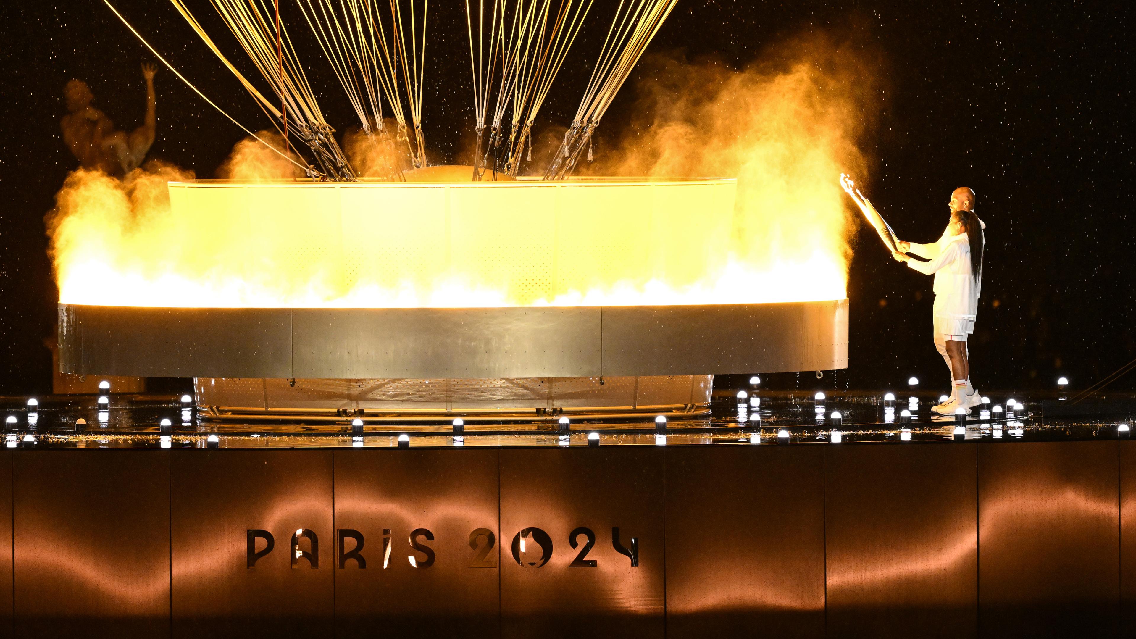 Marie-Jose Perec und Teddy Riner entzünden olympisches Feuer.