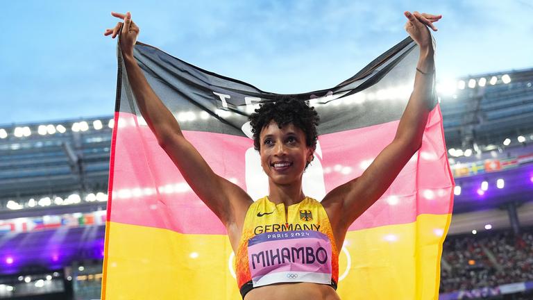 Frau steht im Stadion und hält eine Deutschland Flagge hintersich. 