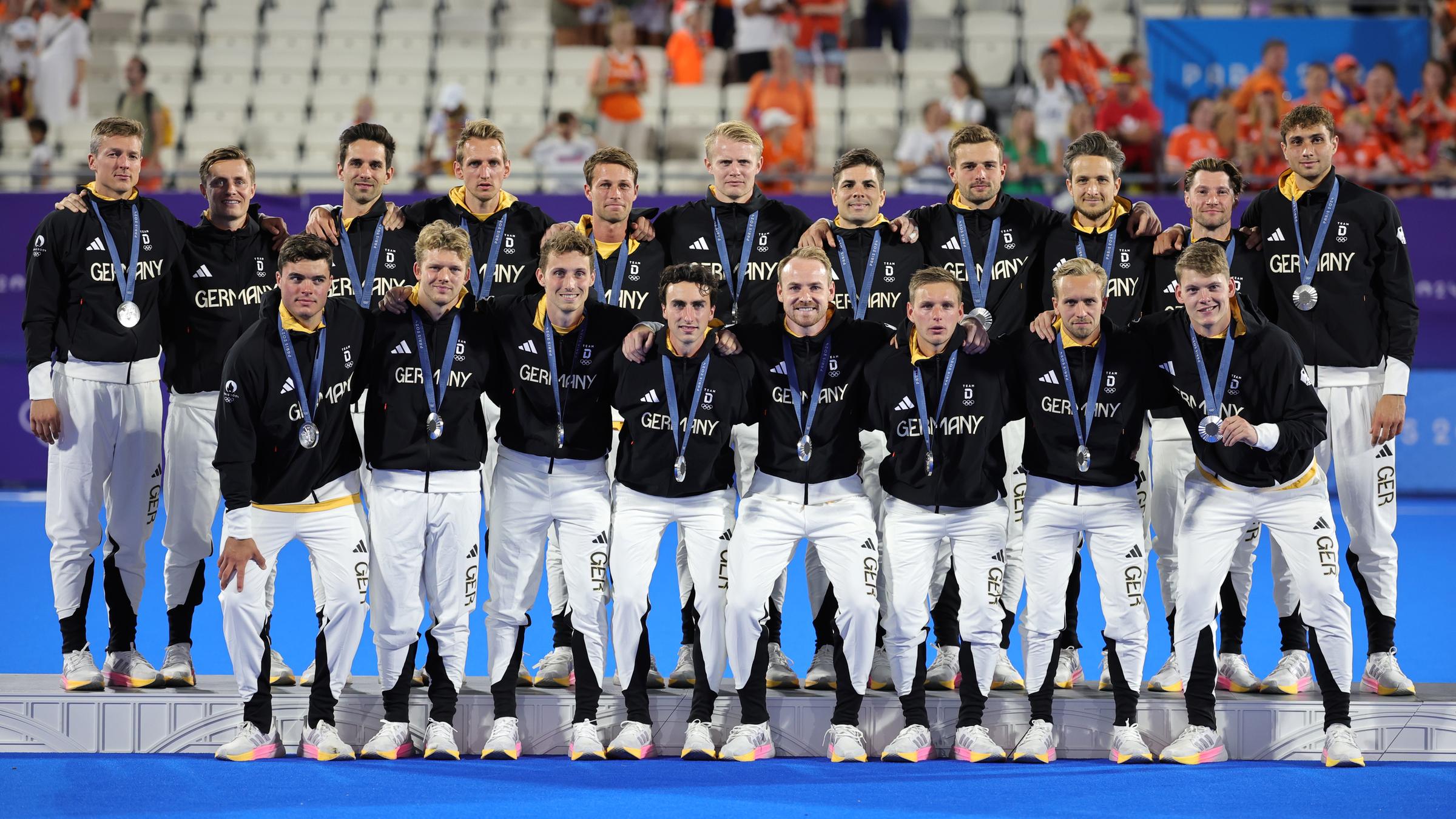 Hockey Manschaft posiert für ein Mannschaftfotos. Die Männer tragen ihre Silbermedaillen. 