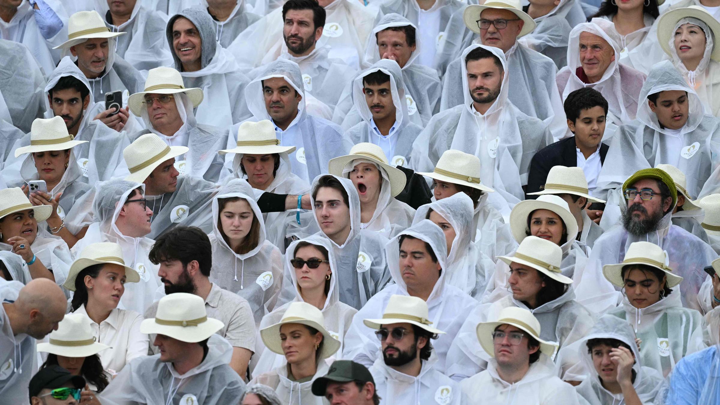 Zuschauer bei der Eröffnungsfeier der Olympischen Spiele tragen Regenjacken.