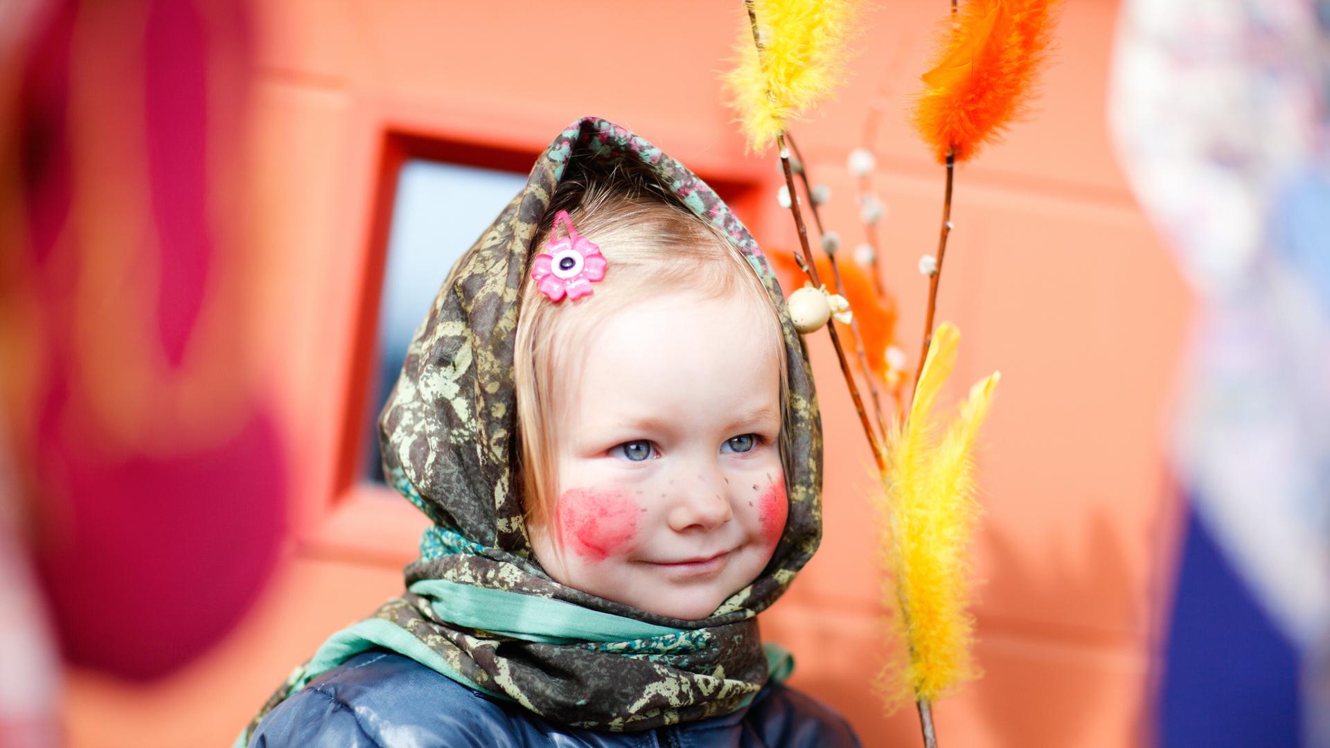 kleines Mädchen ist als Hexe verkleidet und hält bunten Weidenzweig