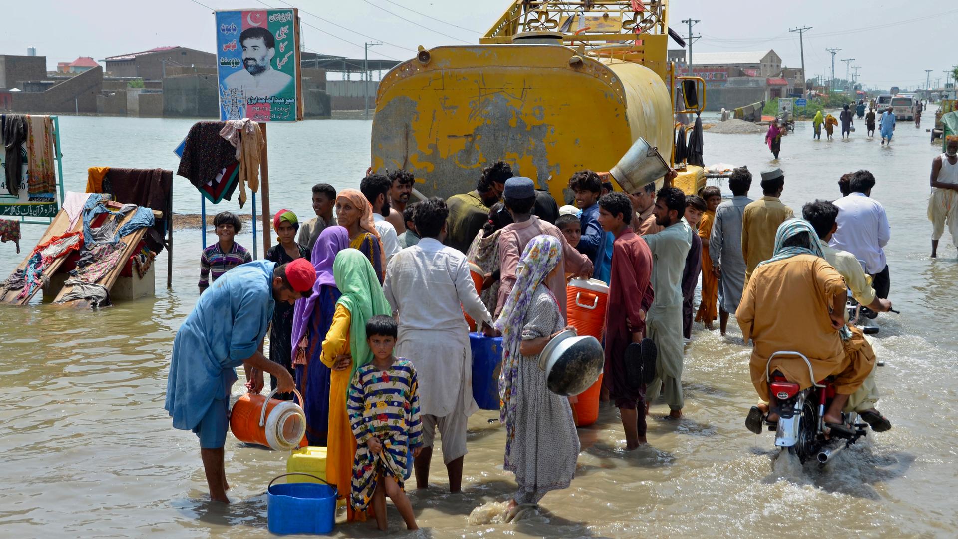 Menschen stehen  auf einer überschwemmten Straße an, um sauberes Trinkwasser zu bekommen.