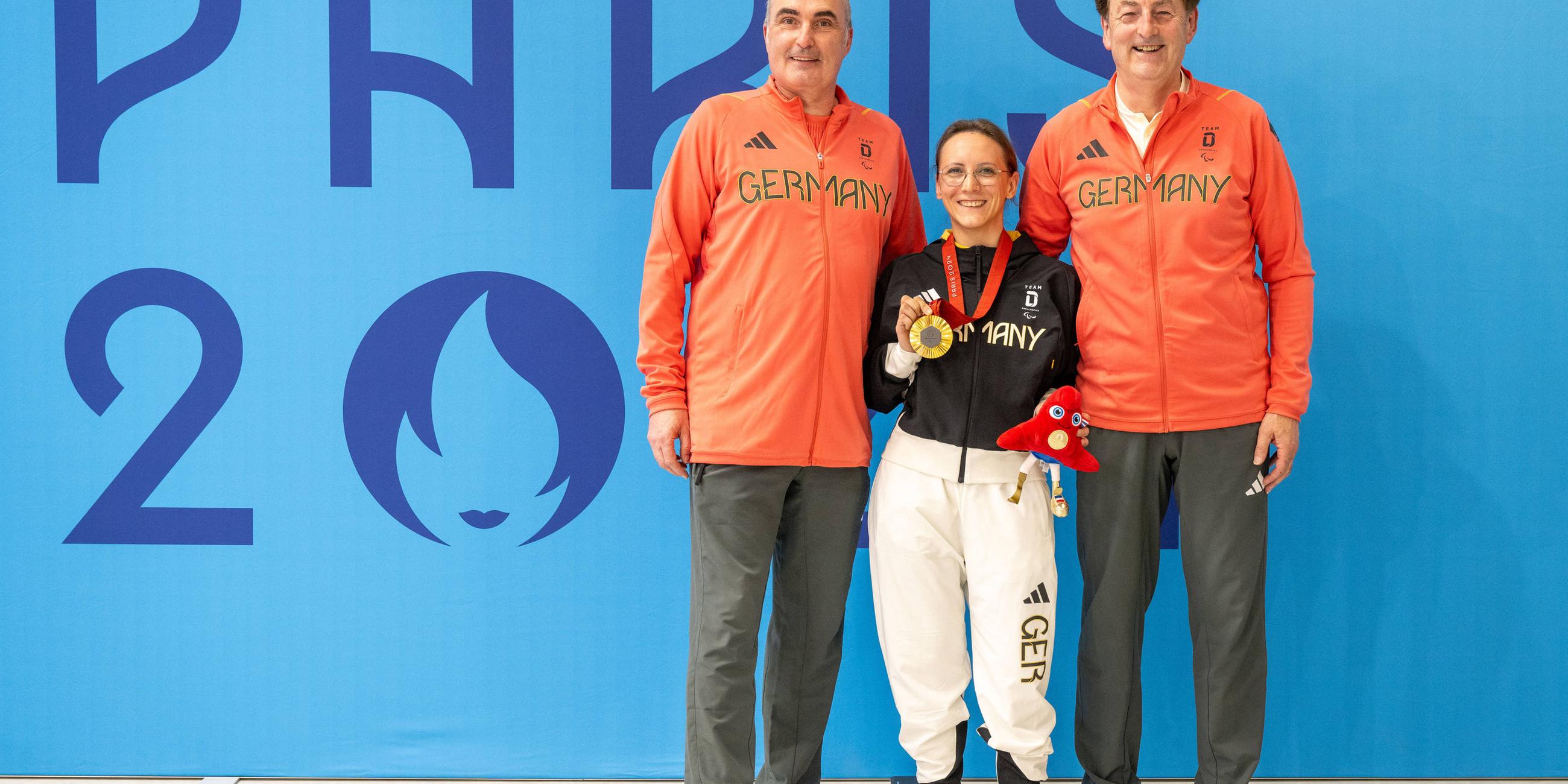 Natascha Hiltrop steht zwischen zwischen ihren beiden Coaches mit der Goldmedaille in der Hand