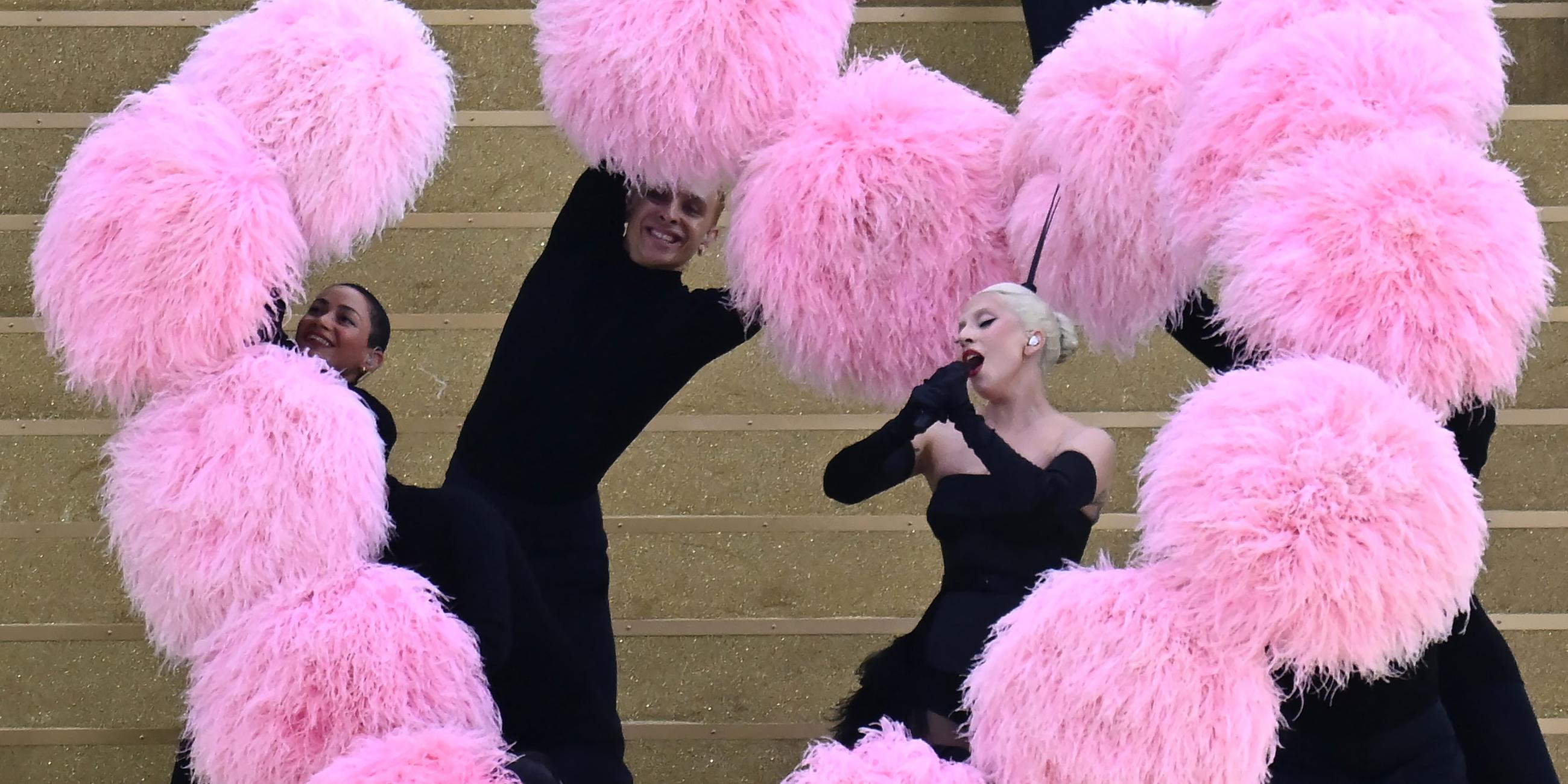 Lady Gaga singt und um sie herum wird ein Herz aus pinkfarbenen Puscheln geformt. 