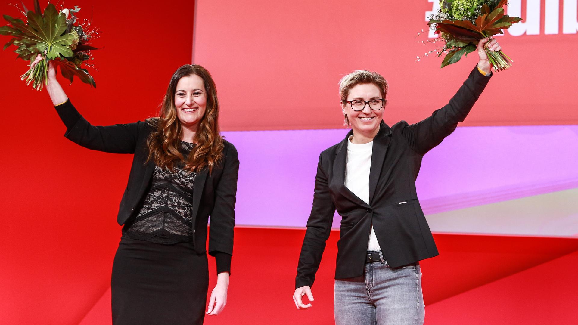 Janine Wissler (links) und Susanne Hennig-Wellsow (rechts) winken mit Blumensträußen.
