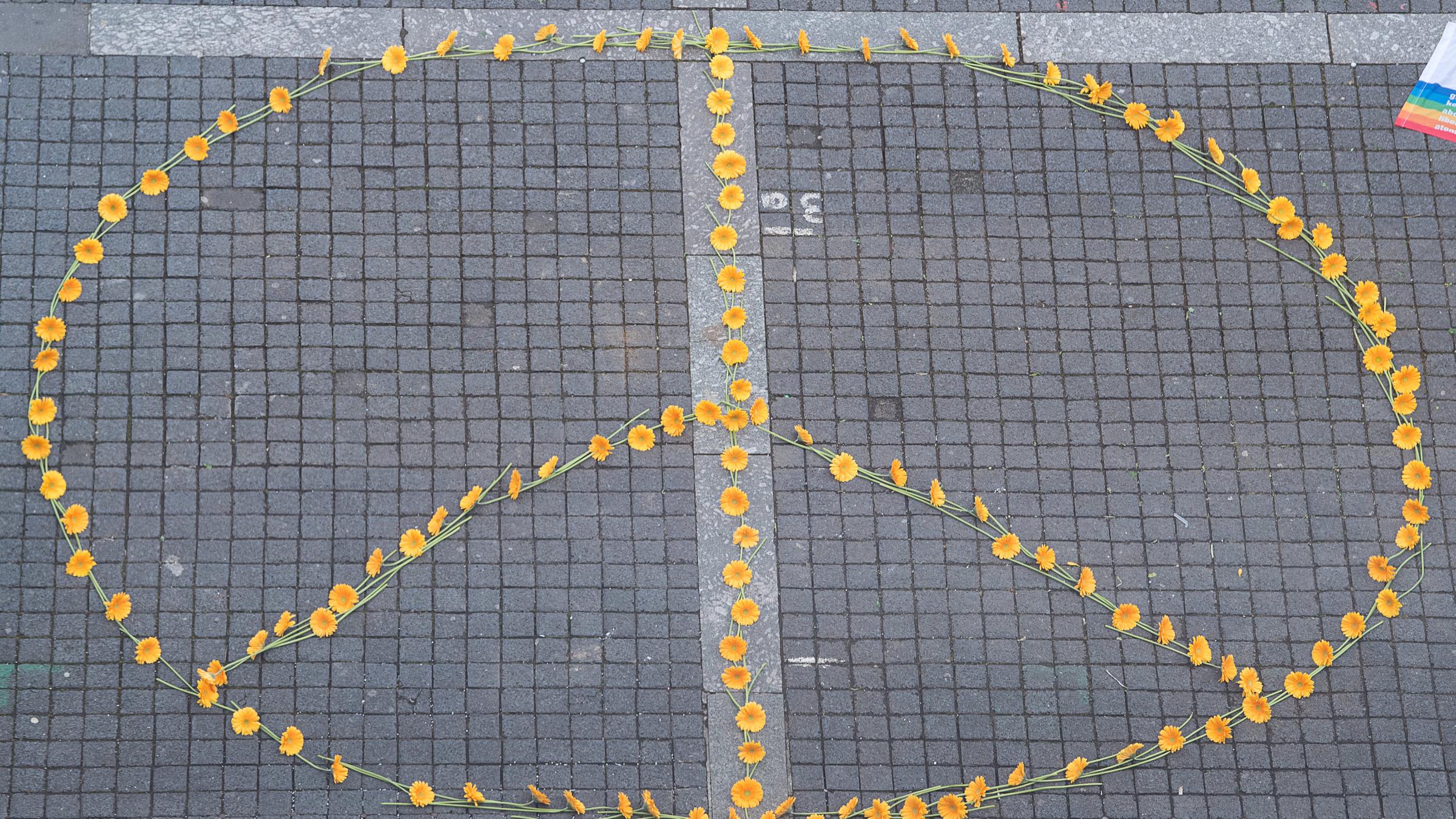 Ein Peace-Zeichen aus Blumen ist auf dem Boden gestaltet. Es besteht aus einem Kreis mit drei Strichen. 