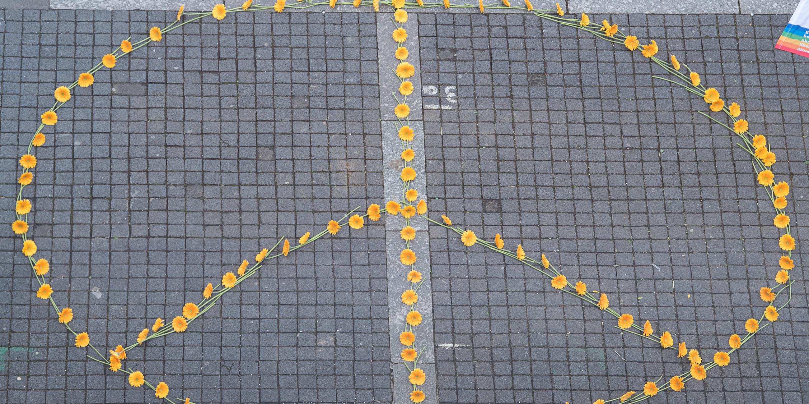 Ein Peace-Zeichen aus Blumen ist auf dem Boden gestaltet. Es besteht aus einem Kreis mit drei Strichen. 