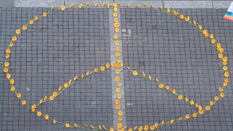 Ein Peace-Zeichen aus Blumen ist auf dem Boden gestaltet. Es besteht aus einem Kreis mit drei Strichen. 