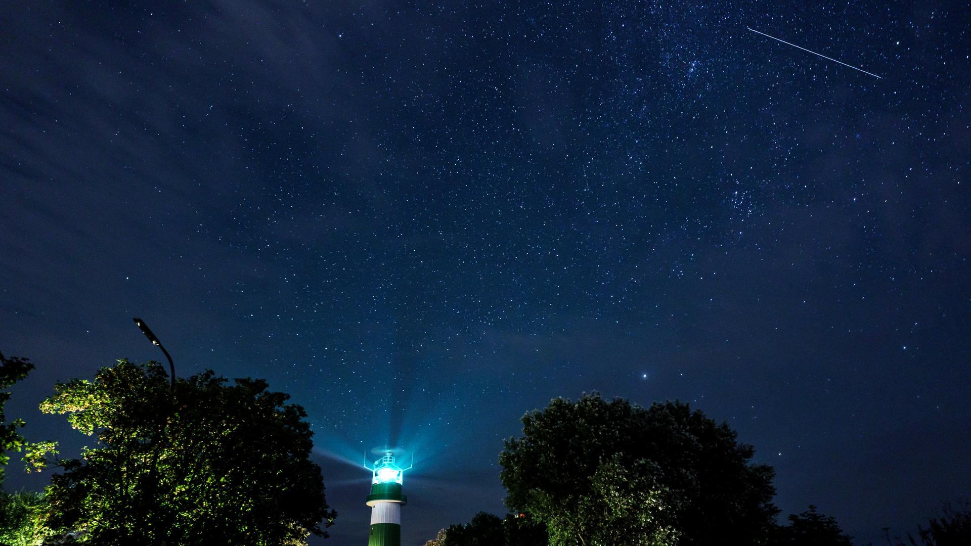 Der Nachthimmel über Deutschland ist mit Sternen und einer Sternschnuppe zu sehen.