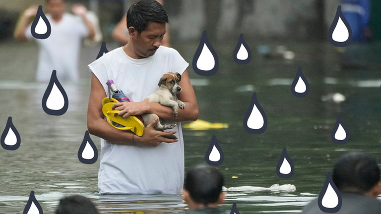 Ein Mann trägt einen Hund auf dem Arm und watet mit ihm durch eine überflutete Straße. 