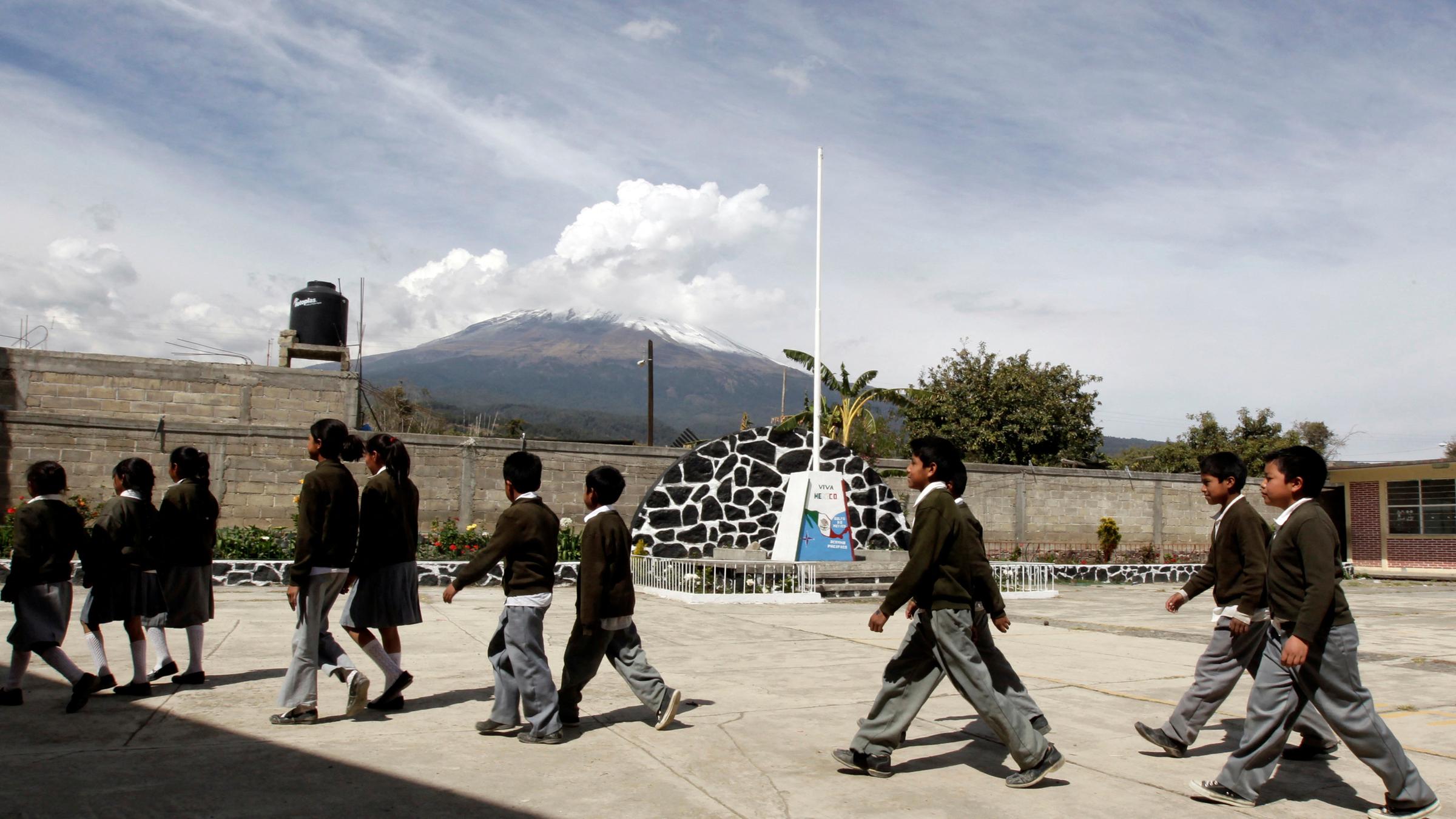 Schülerinnen und Schüler üben für eine Evakuierung, im Hintergrund ist der rauchende Vulkan zu sehen.