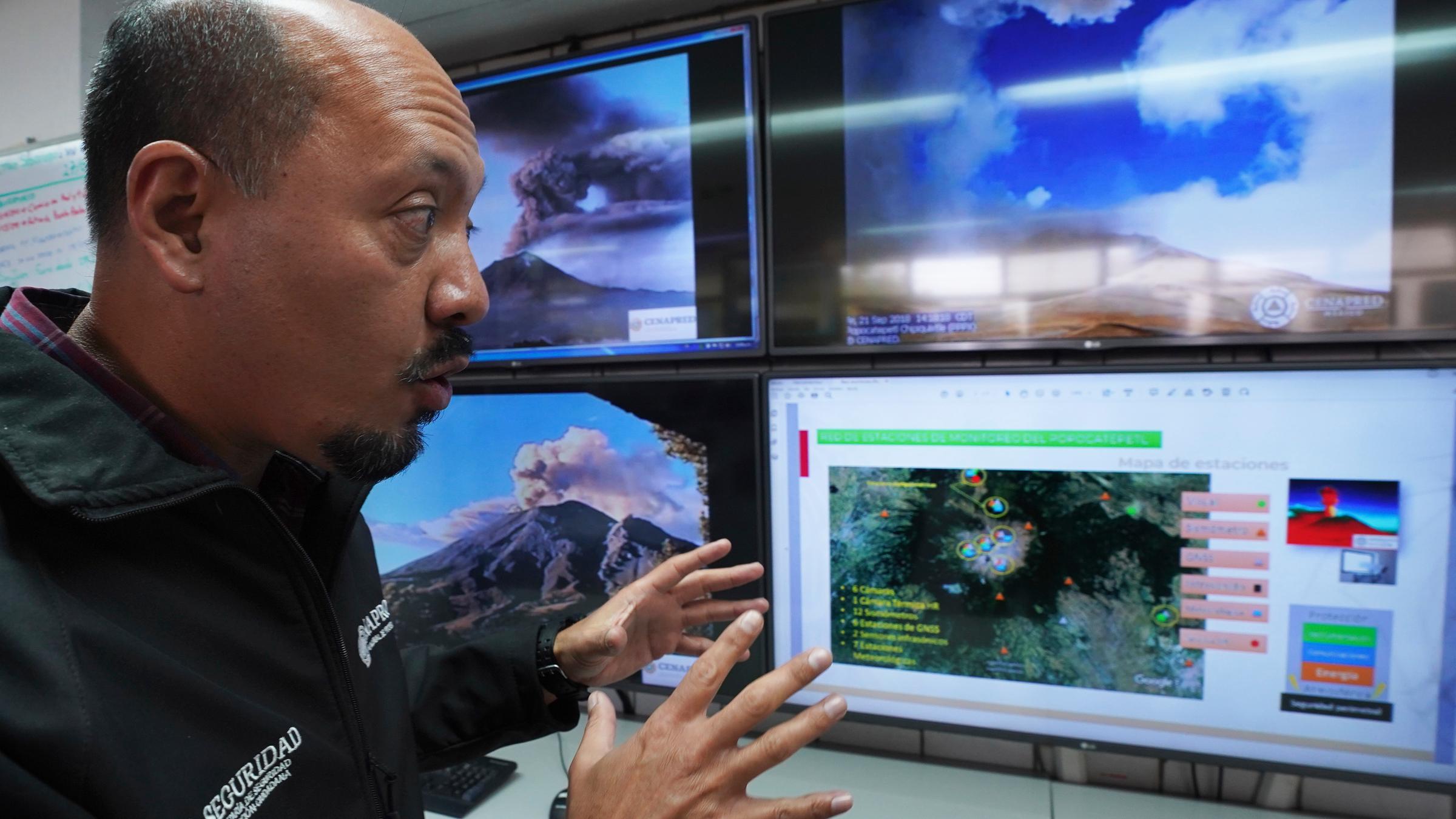 Ein Mann sitzt vor vielen Überwachungsbildschirmen mit dem Vulkan drauf.