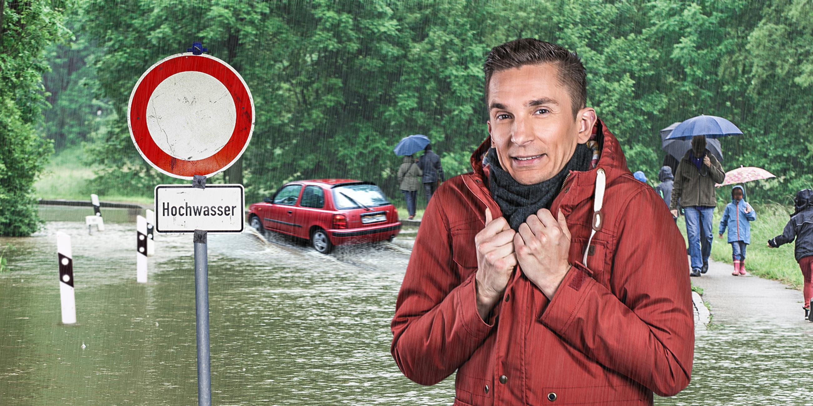 Moderator Eric Mayer steht mit angespannter Miene neben einem Schild mit der Aufschrift "Hochwaser". Im Hintergrund laufen Menschen mit Regenschirmen und es fährt ein Auto durchs Wasser auf einer überfluteten Straße.