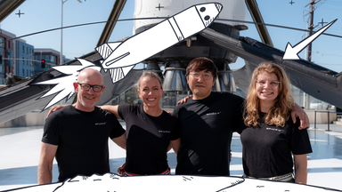 SpaceX-Team vierköpfig. Ganz rechts lächelnd Rabea Rogge. Darüber Grafiken von Rakete und Pfeil auf Rabea. 
