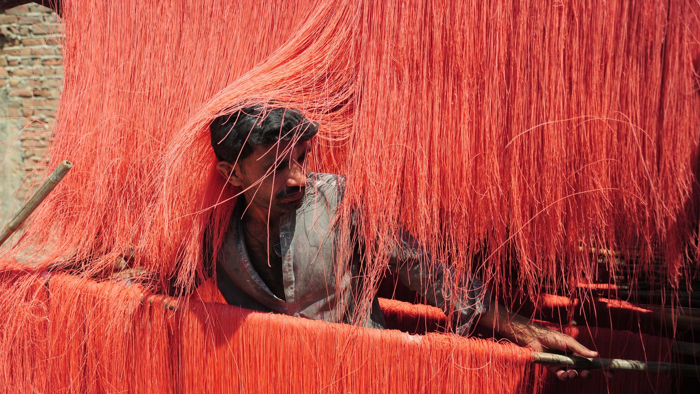 Ein Arbeiter bereitet rote Vermicelli Pasta zu. Sie hängt in langen roten Fäden von Holzstangen.