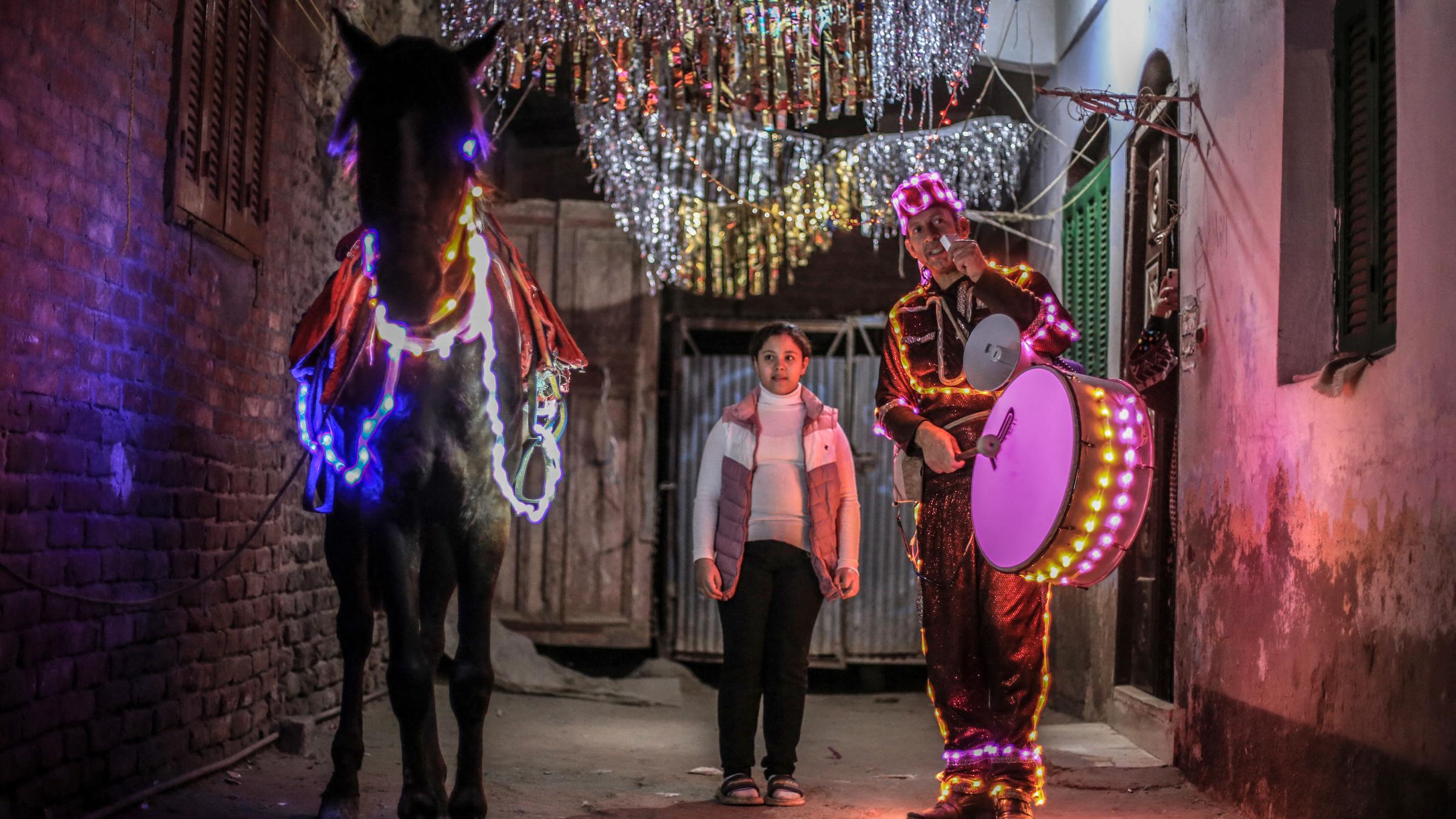 Ein Trommler und sein Pferd laufen beleuchtet mit LED-Ketten durch die nächtlichen Straßen Kairos.