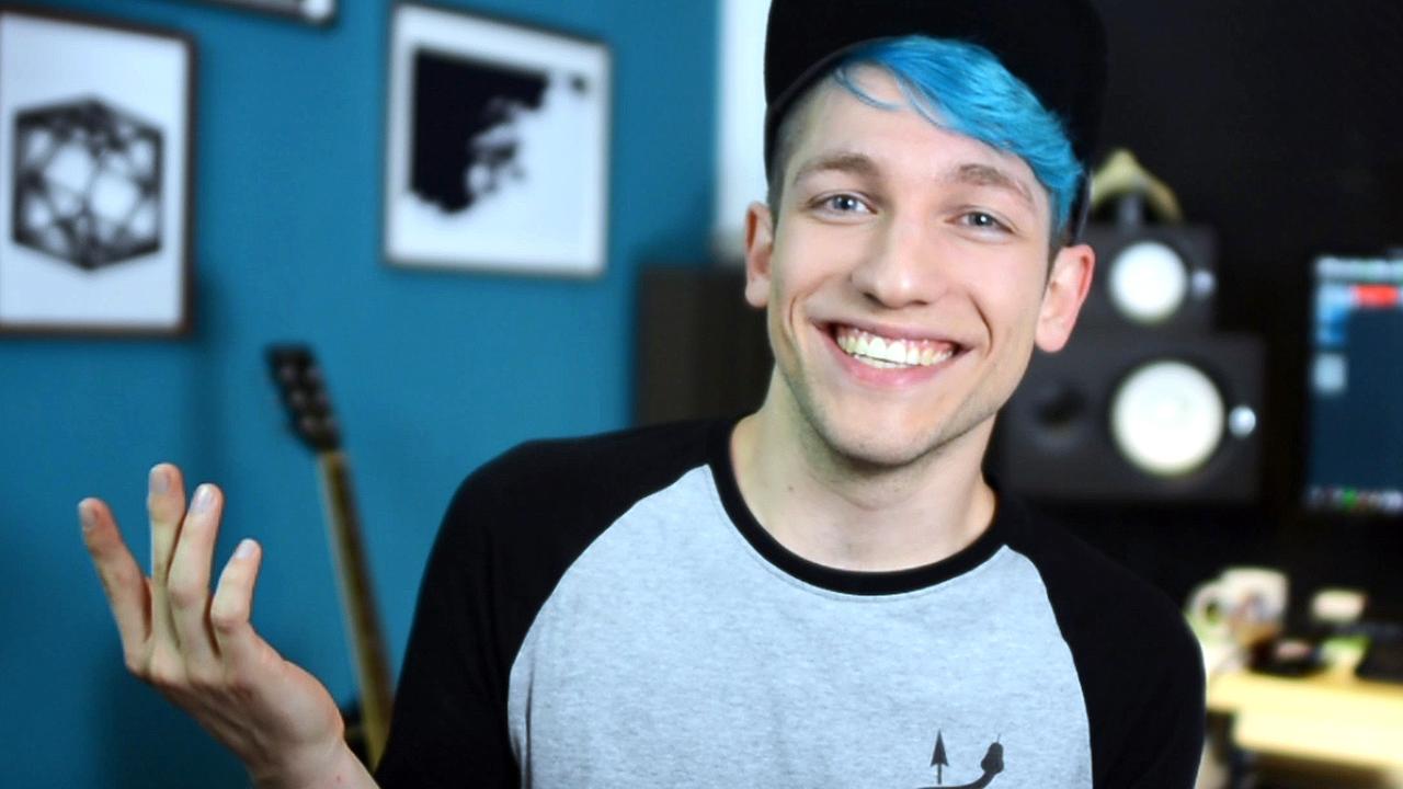 Junger Mann mit blauen Haaren steht vor einem PC im Hintergrund