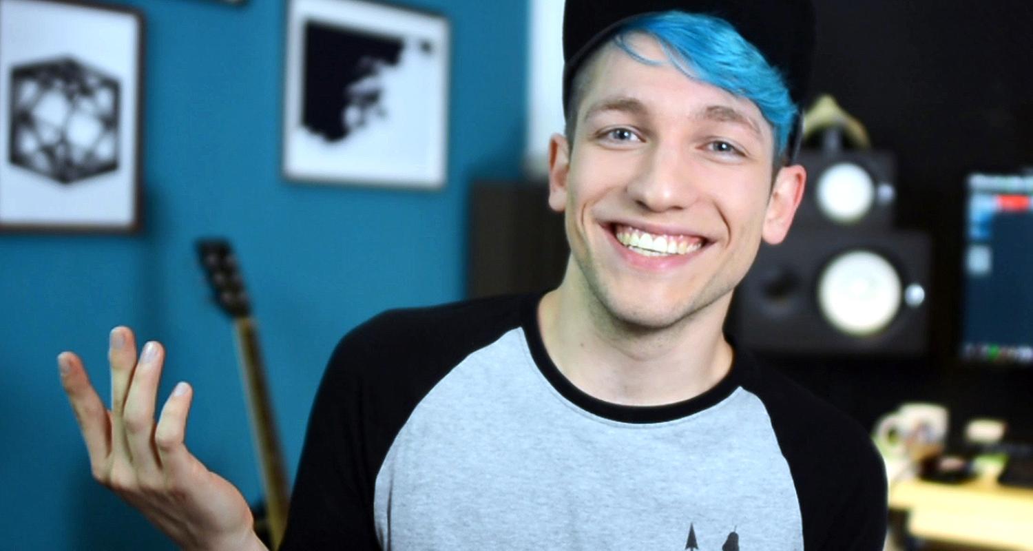 Junger Mann mit blauen Haaren steht vor einem PC im Hintergrund