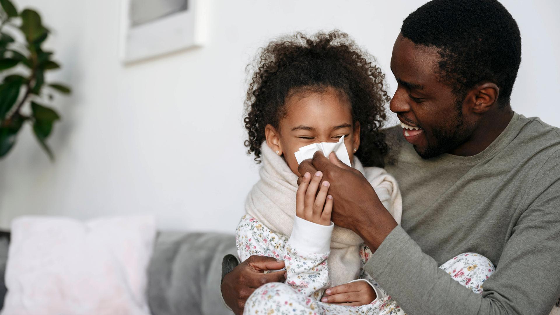Ein Kind sitzt auf dem Schoß ihres Vaters und kriegt von ihm die Nase geputzt