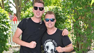 DJ Robin und Schürze stehen nebeneinander vor einem Gebüsch.