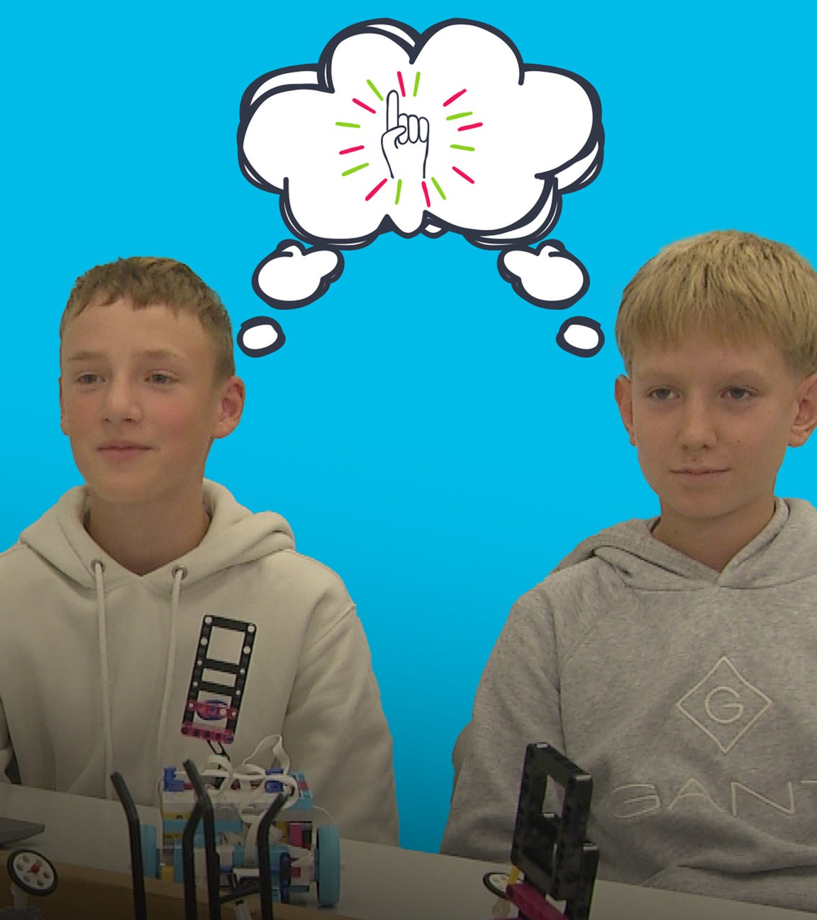 Zwei Jungs aus Bingen sitzen am Schreibtisch mit ihren Robotern, zwischen ihnen grafische Sprechblase mit Idee-Symbol  