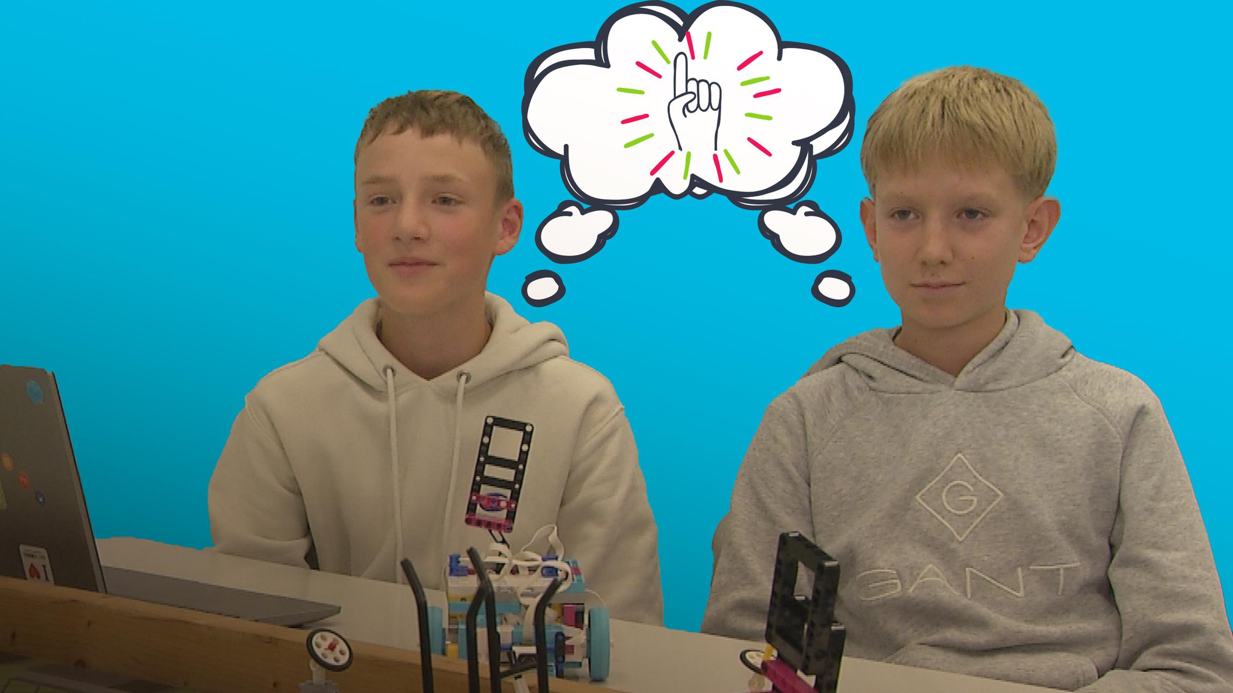 Zwei Jungs aus Bingen sitzen am Schreibtisch mit ihren Robotern, zwischen ihnen grafische Sprechblase mit Idee-Symbol  