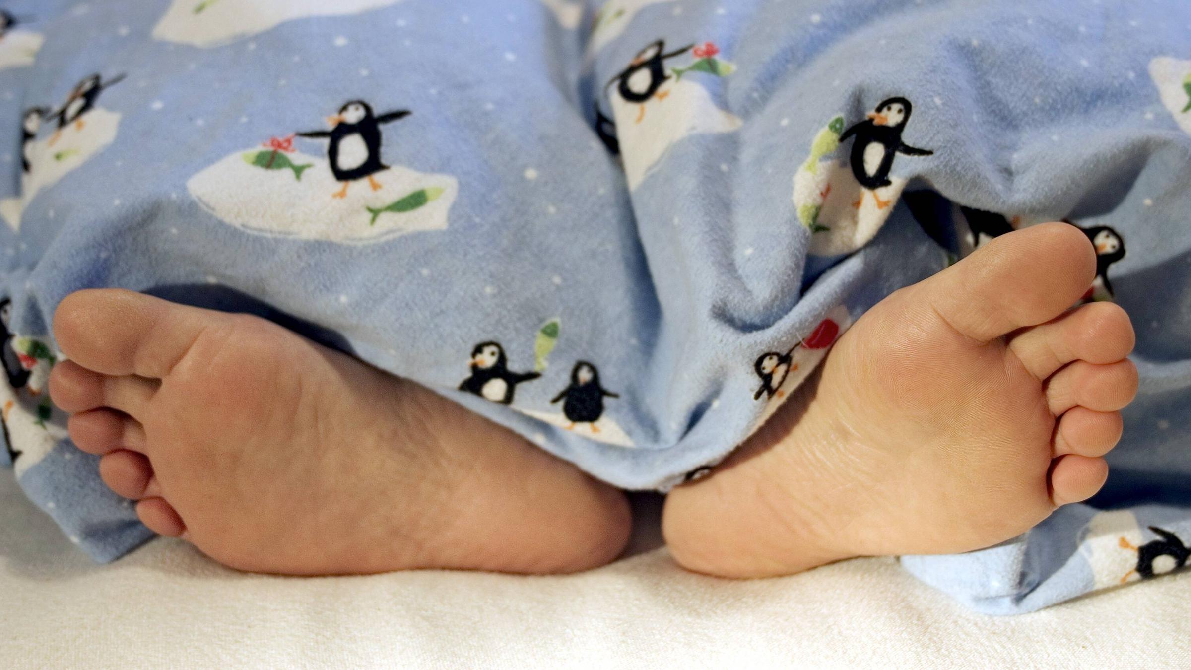 Nackte Füße unter der Bettdecke.