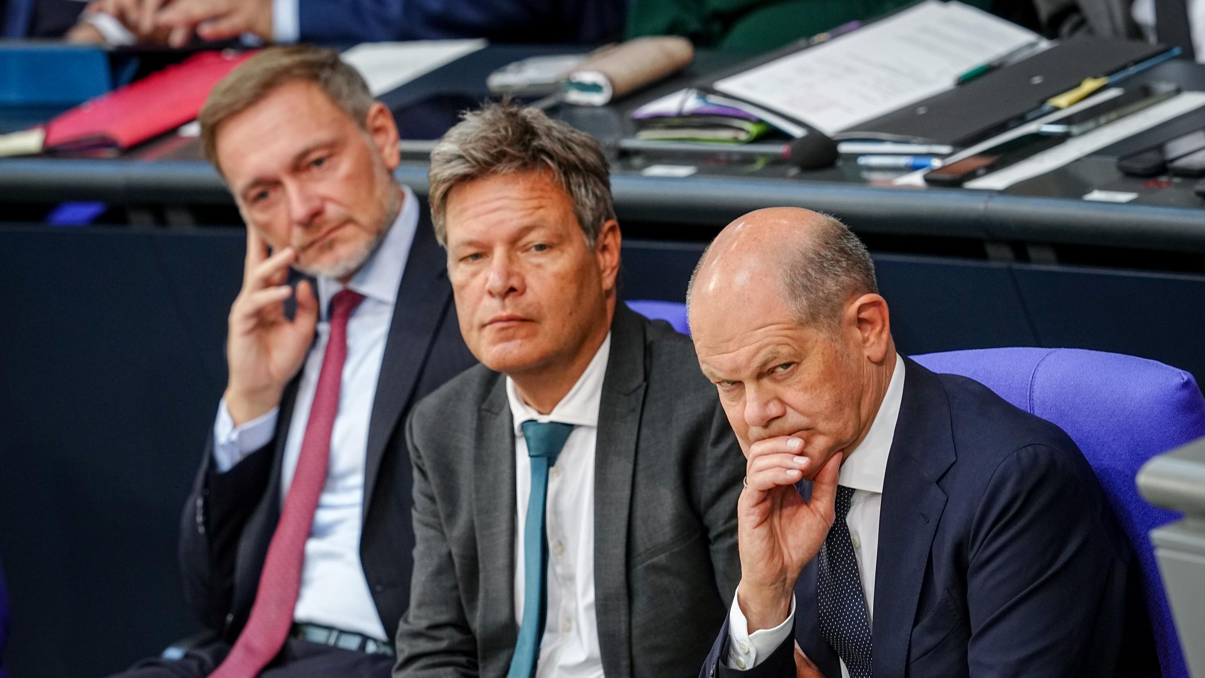 Lindner, Habeck und Scholz sitzen nebeneinander im Bundestag und schauen kritisch.