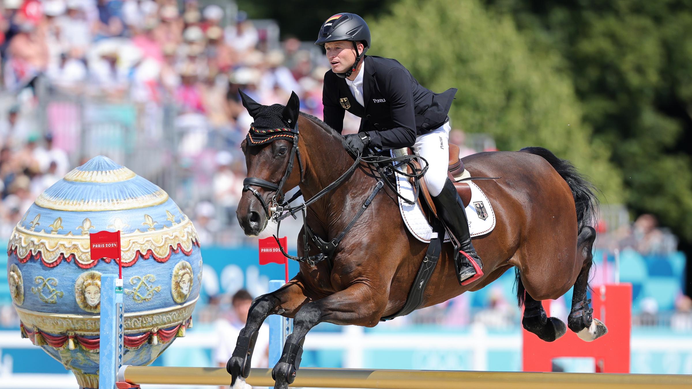 Reiter Michael Jung springt mit seinem dunkelbraunen Pferd über ein Hindernis.