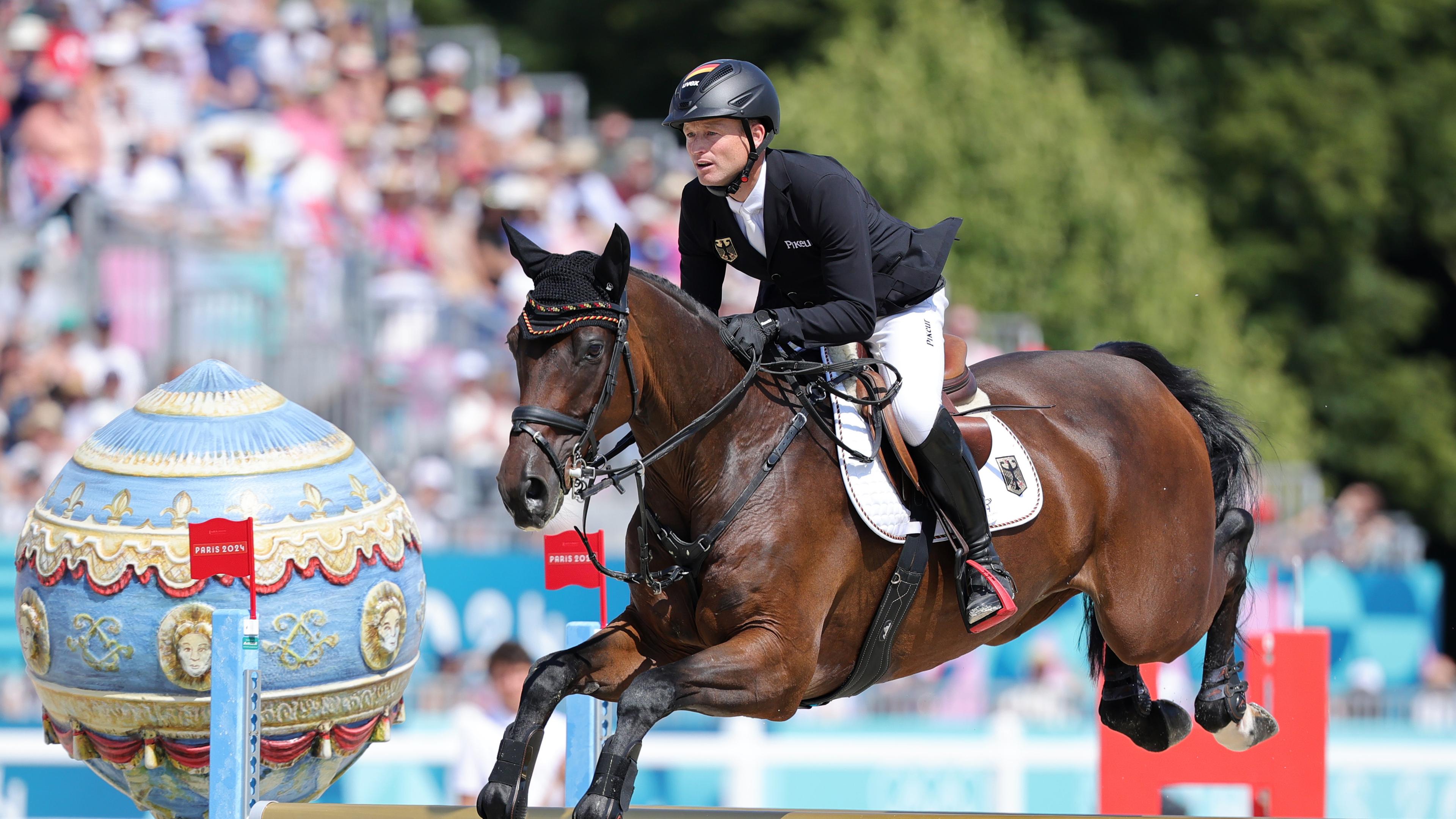 Reiter Michael Jung springt mit seinem dunkelbraunen Pferd über ein Hindernis.