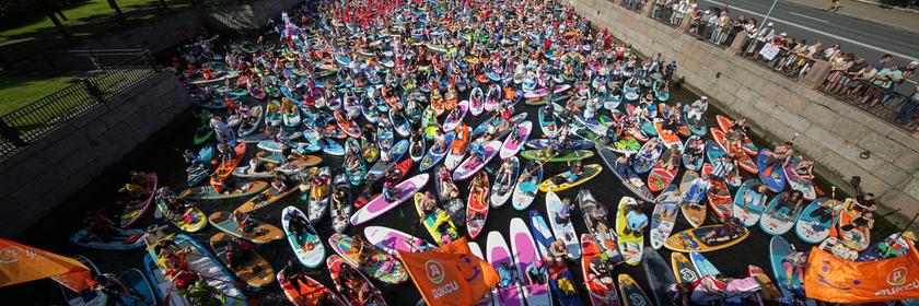 Bei einem Festival in St. Petersburg, Russland, paddeln viele Menschen auf ihren Stand-up-Paddle-Boards über einen Fluss. Und schaut mal genauer hin: Viele haben sich dafür richtig kreativ verkleidet! 😄