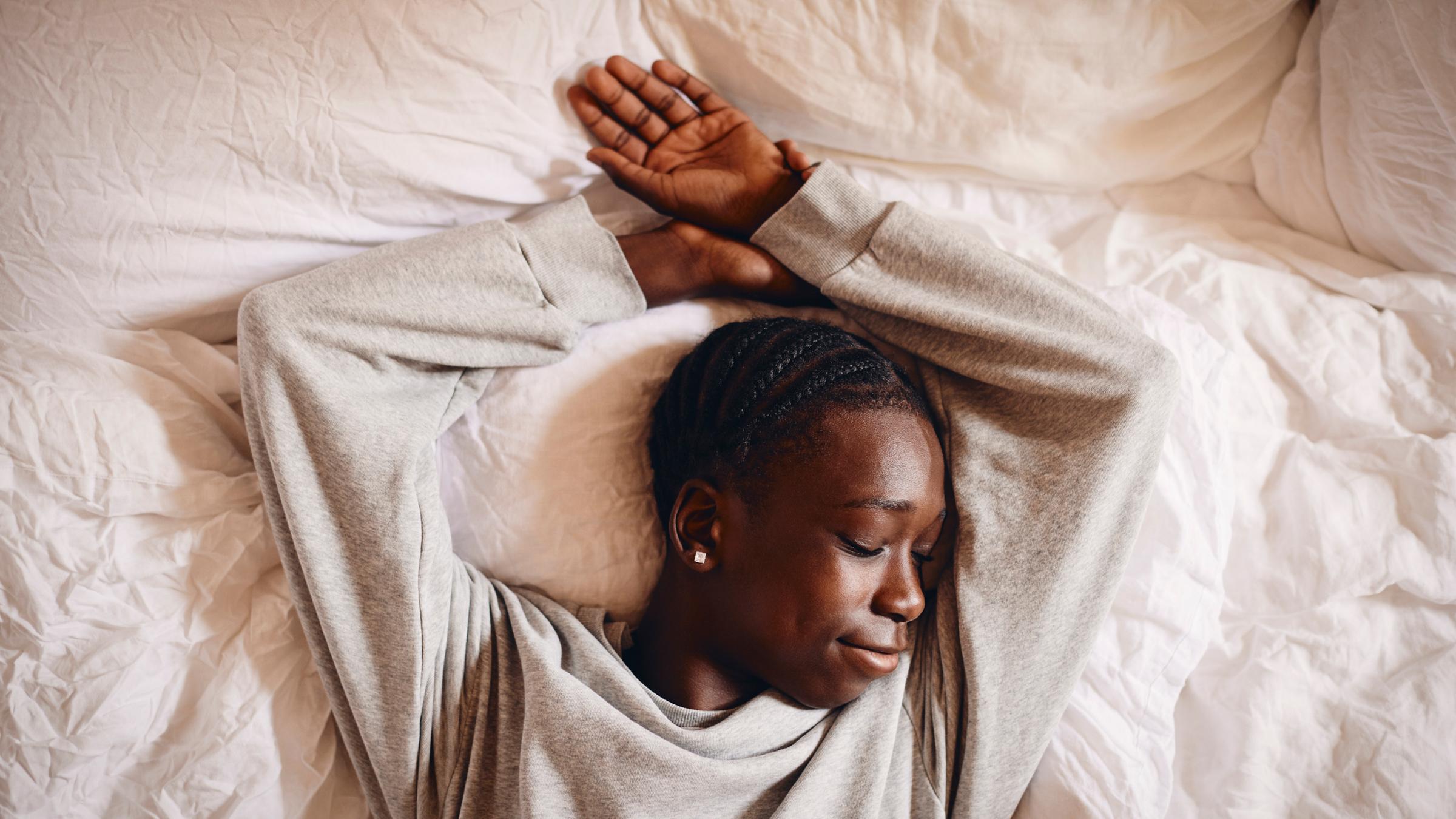Seitenansicht eines jungen Mädchens, das friedlich in einem hellen Bett schläft und sich unter einer weißen Bettdecke an einen flauschigen Stoffhasen kuschelt.