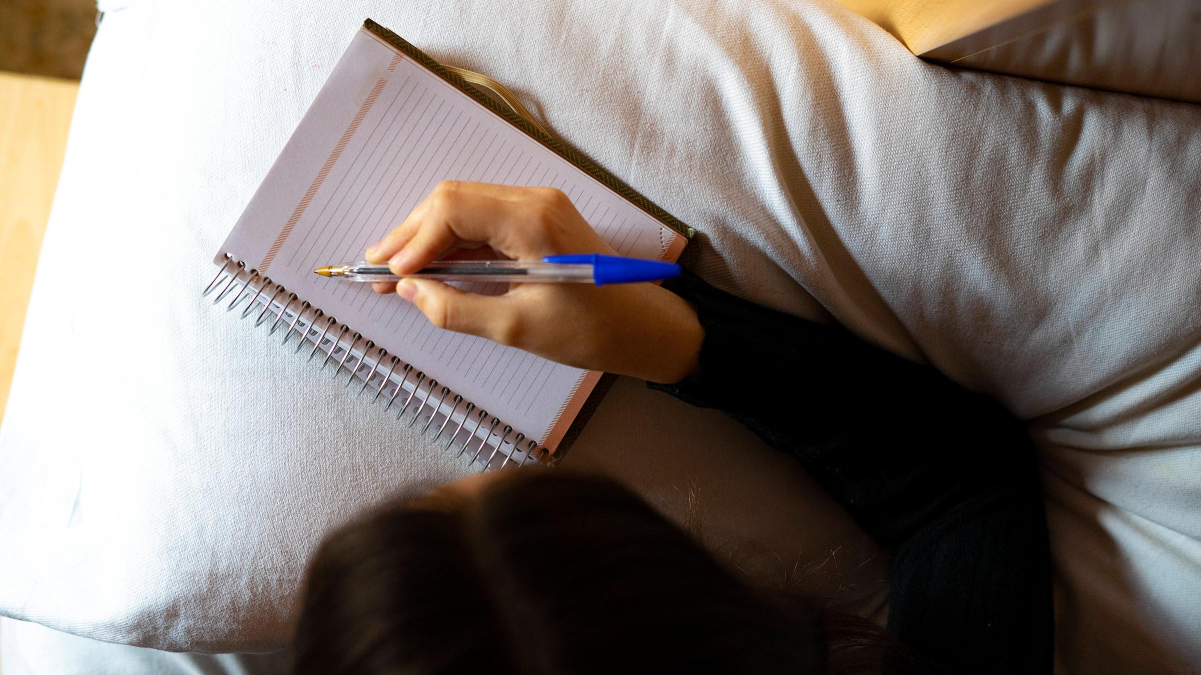 Vogelperspektive Frau, die im Bett in Heft schreibt