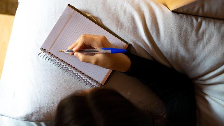 Vogelperspektive Frau, die im Bett in Heft schreibt