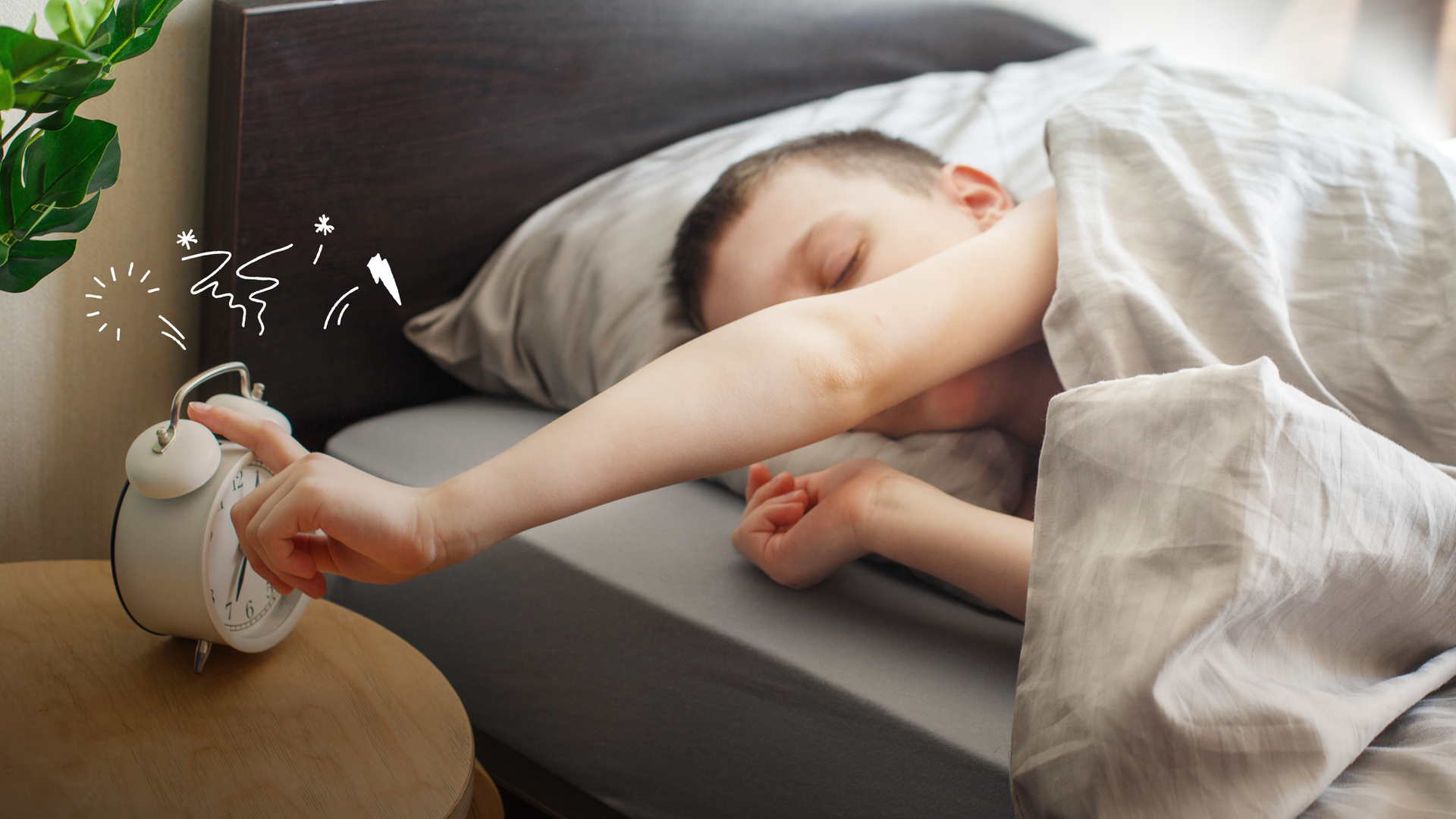 Ein Kind liegt im Bett und drückt auf den Wecker. 
