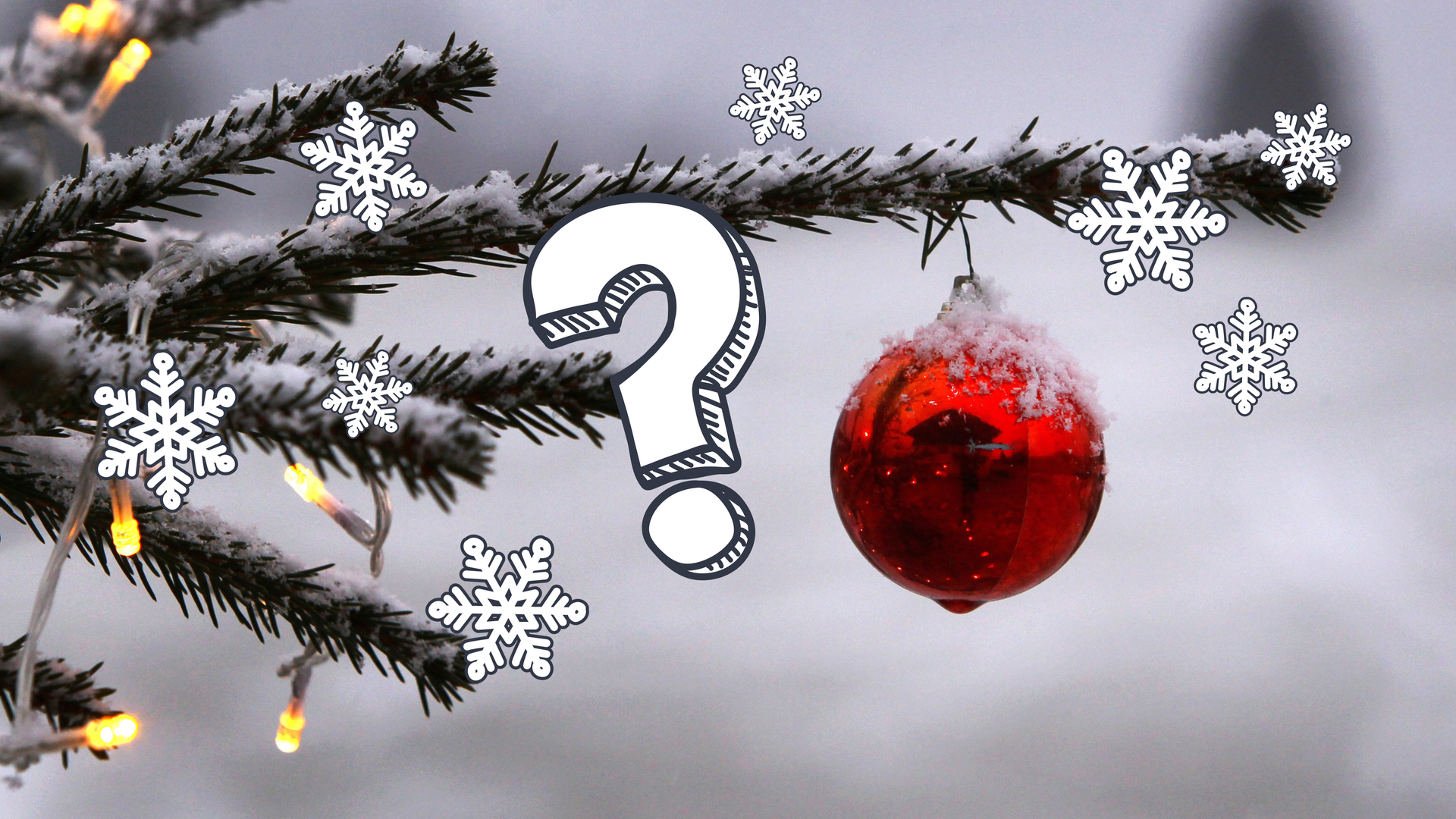 Eine rote Weihnachtskugel hängt mit Schnee bedeckt an einem Tannenbaumzweig und einer Lichterkette