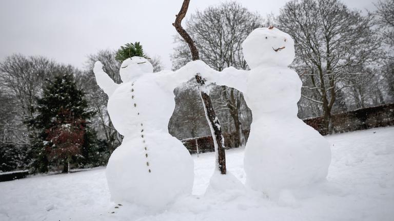 Zwei Schneemänner im Schnee. Sie halten Händchen.
