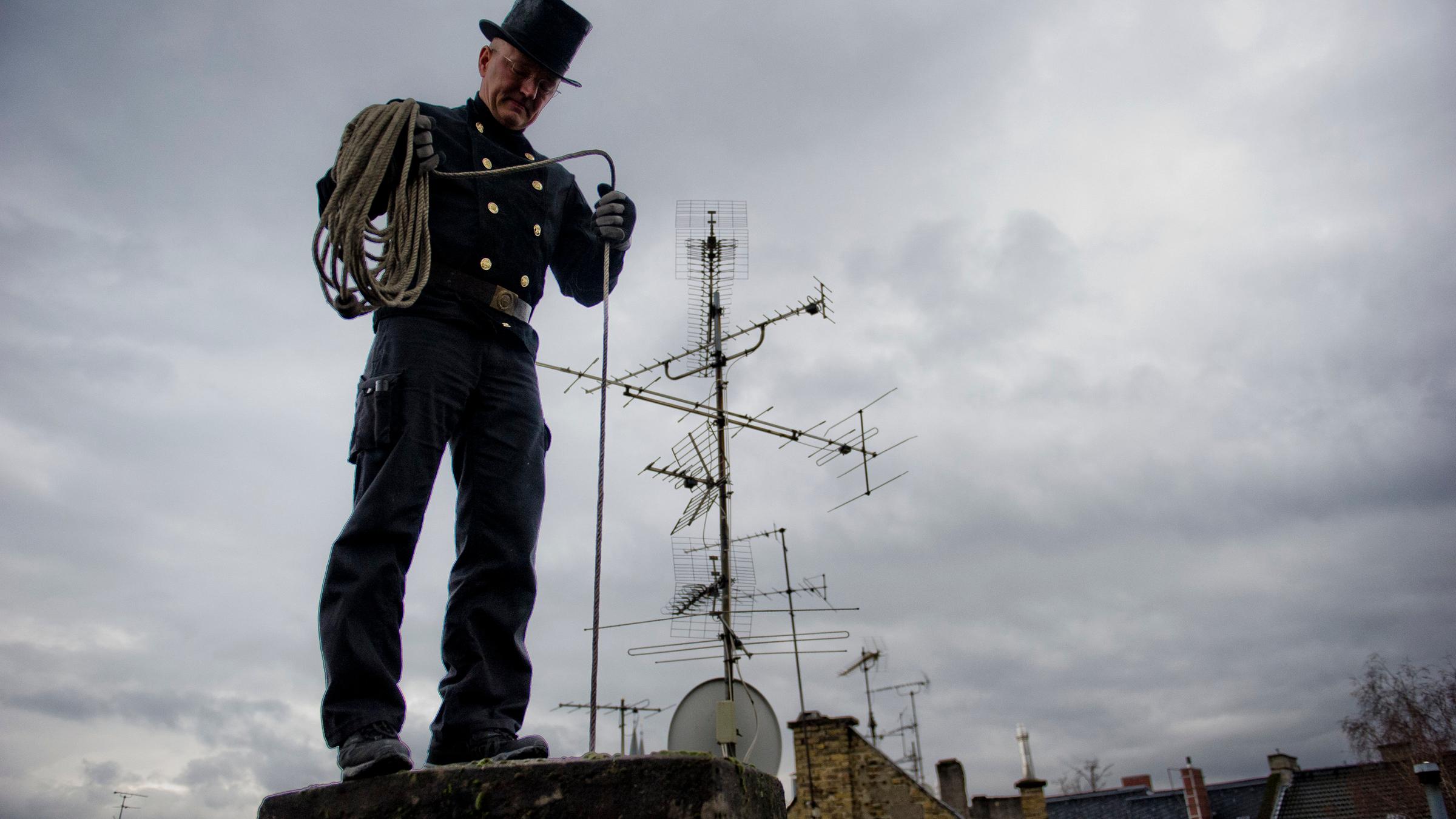 ein Schornsteinfeger reinigt einen Schornstein auf dem Dach