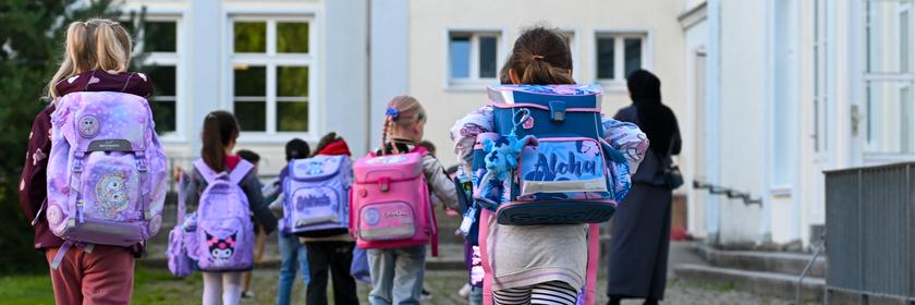 Kinder mit Schulranzen gehen in Richtung Gebäude.
