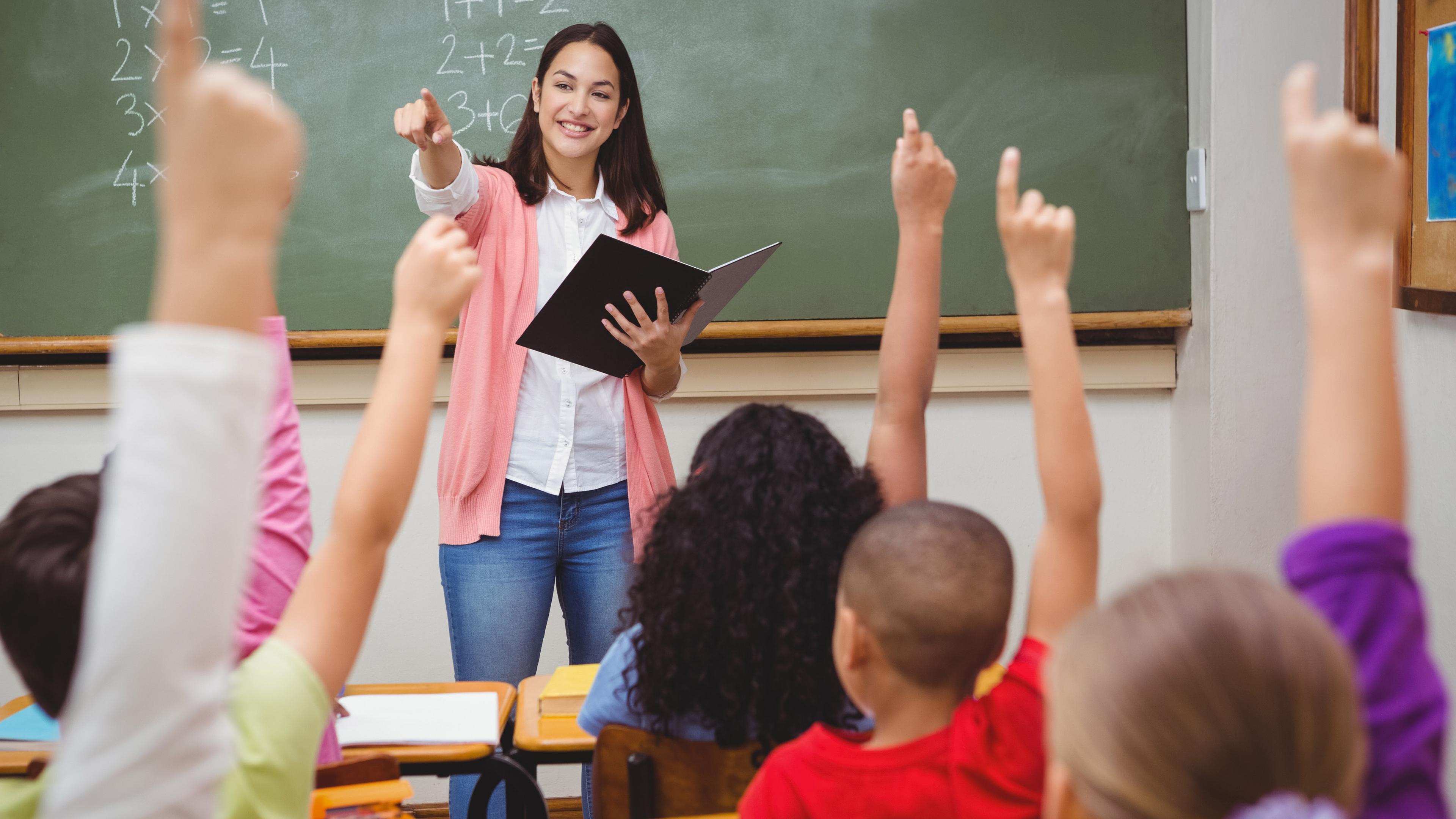 Schüler im Vordergrund, Lehrerin im Hintergrund. Schüler melden sich. 
